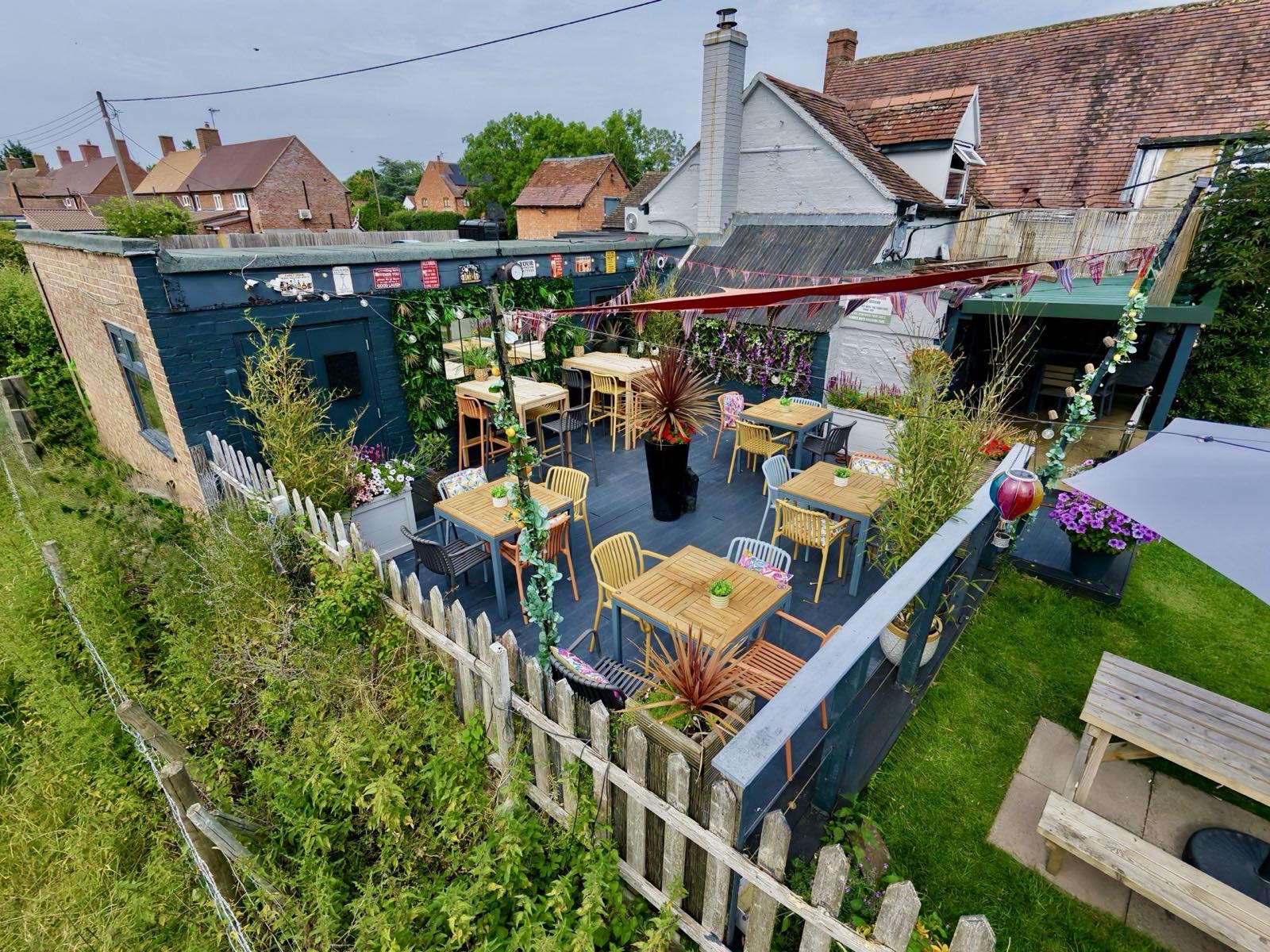 Elevated view of the secret garden decked terrace at The Masons Arms, with colourful chairs, bunting, planters and string lights.